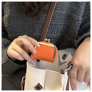 Close-up of an orange pebble leather mini pouch with gold kiss-lock clasp on a white tote bag