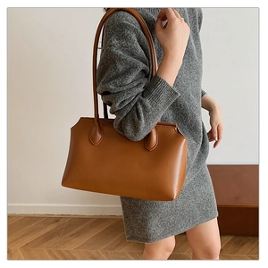 Detail of a brown leather tote bag with long straps worn on a grey knitted dress