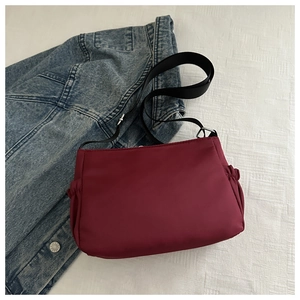 Detail view of burgundy nylon crossbody bag with elastic side pockets and canvas strap