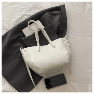 Detail of white pebble leather bucket bag paired with gray suit in lifestyle setting