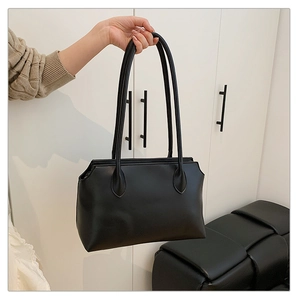 Close-up of a black minimalist tote bag held by a person against a modern interior background