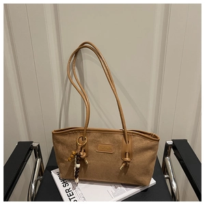 Detail of a brown suede tote bag with FASHION embossing and a beaded keychain accessory