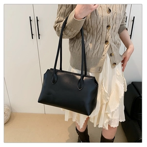 Detail of black glossy leather tote bag worn by a model in a minimalist chic outfit