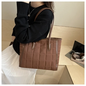 Detail of coffee brown quilted tote bag showing square stitching and leather strap