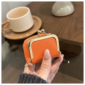 Mini orange pebble leather coin purse with vintage gold clasp held in hand at a cafe