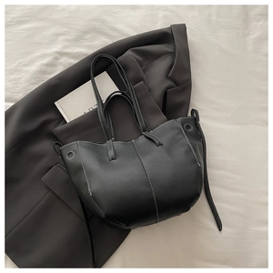 Detail of black lychee-textured leather bucket bag with contrast stitching on blazer