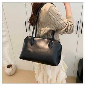 Detail of black leather tote bag with wavy top edge worn by model in a modern room