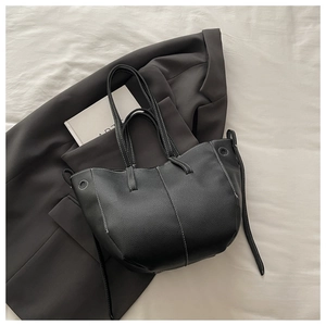 Detail of black lychee leather bucket bag with contrast white stitching on gray blazer