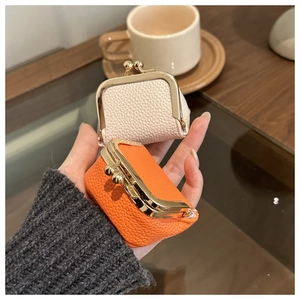 Mini lychee leather jewelry pouch with gold clasp held by hand in cream and orange