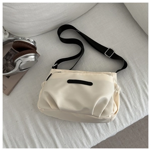 Detail of minimalist cream crossbody bag with adjustable black strap and side pocket