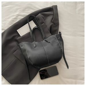 Close-up of black lychee grain bucket bag with contrast white stitching and art book