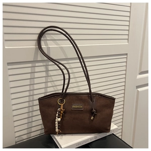 Detail of dark brown suede tote bag featuring a beaded charm and fashion patch