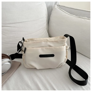 Detail of beige nylon crossbody bag featuring adjustable black strap and logo patch