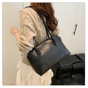 Minimalist black matte tote bag with slim straps shown on model in a modern home setting