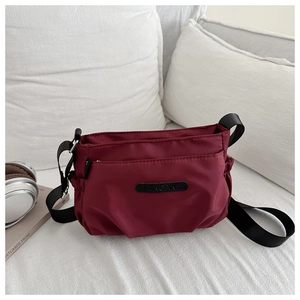 Close-up of dark burgundy nylon crossbody bag with JINGPIN patch and storage pockets