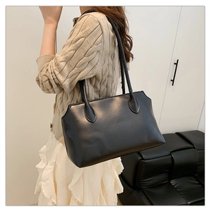 Side view of a large black matte leather tote bag worn by a model in a minimal setting