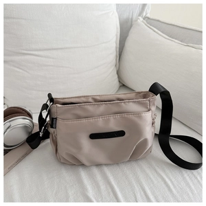 Detailed close-up of beige nylon pleated shoulder bag with black logo and strap on white fabric