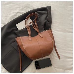 Close-up of brown pebbled leather tote with white contrast stitching on a bed