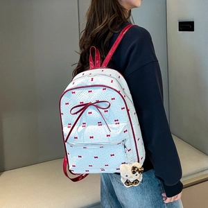Detailed view of polka dot backpack with red bow and plush kitty keychain on model