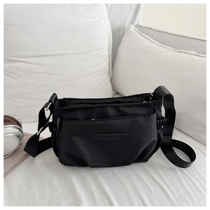 Detailed view of black nylon shoulder bag with adjustable strap on white bedding