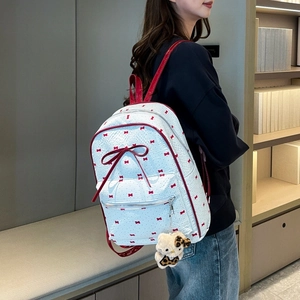 Detailed side view of white bow-patterned backpack with adjustable red straps and charm