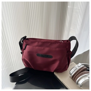Detailed view of a burgundy nylon crossbody bag featuring a black adjustable strap and patch