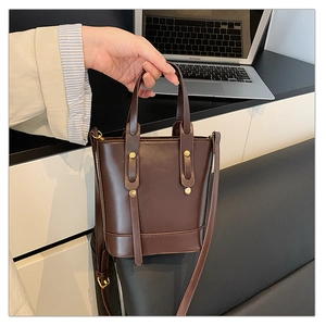 Detailed shot of a dark brown bucket bag featuring gold rivets and refined stitching