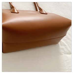Close-up of brown leather tote bag with fine stitching and tubular handles