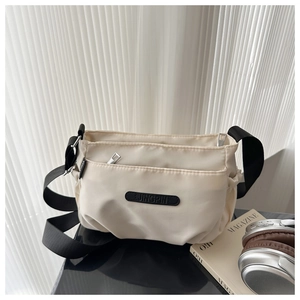 Detail of beige nylon crossbody bag with multi-zipper pockets and black strap on a desk