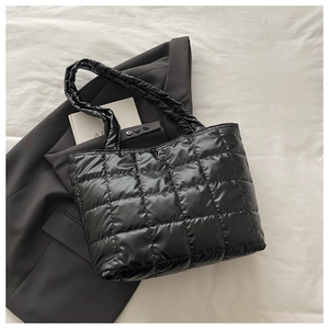 Detail of black quilted puffer tote bag with glossy nylon texture and wide strap