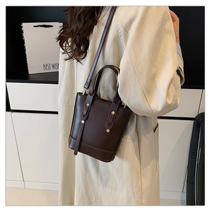 Detail of dark chocolate leather bucket bag with gold rivets and long shoulder strap