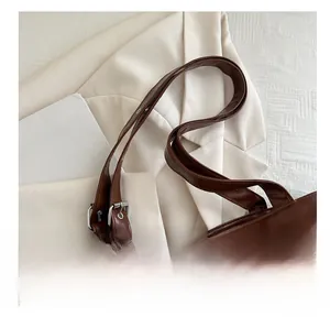 Detail of a brown tote bag featuring wide shoulder straps and silver adjustable metal buckles