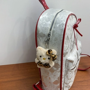 Detail of white textured backpack with red trim and cute plush cat charm decoration