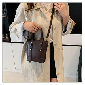 Detail of dark brown leather bucket bag with gold studs shown on a shoulder strap