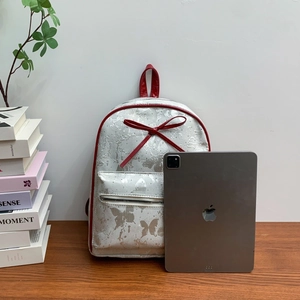 Mini white backpack with silver butterfly pattern, red bow detail, and iPad for scale