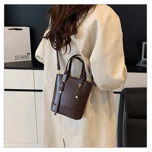Close-up of dark brown bucket bag showing gold metal rivets and adjustable shoulder strap