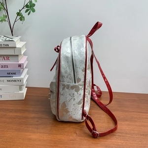 Detail view of cream backpack with silver floral patterns and vibrant red trim on wood