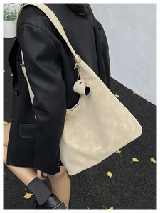 Detail of a cream faux leather tote bag with wide shoulder strap and brand lettering
