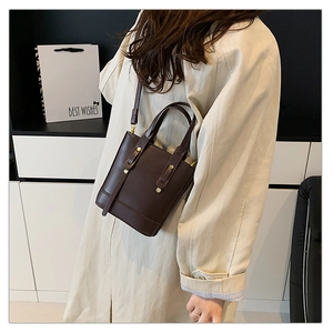Detail of dark brown leather bucket bag with top handles and cross-body strap shown on model