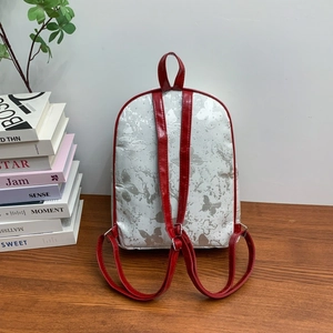 Detail view of silver butterfly-embossed backpack with red contrast shoulder straps