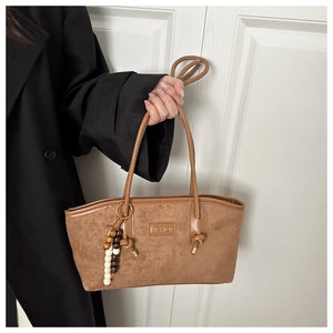 Detail of brown suede tote bag with golden metal plate and retro beaded charm accessory
