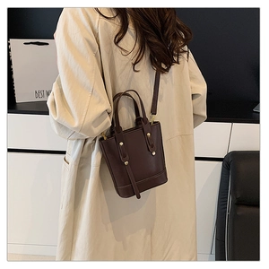 Detail view of deep brown bucket bag with gold rivets and leather crossbody strap