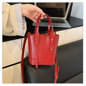 Détail du sac seau en cuir rouge avec doubles poignées et bandoulière réglable