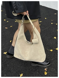 Detail of a large beige suede tote bag with a matching detachable pouch on autumn leaves