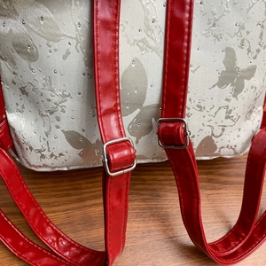 Close-up of red patent leather straps and silver metal buckles on a butterfly backpack