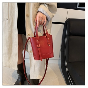 Detail of red leather bucket bag featuring dual handles and adjustable shoulder strap