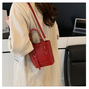 Red PU bucket bag with gold hardware paired with a beige trench coat for a stylish look