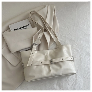 Detail showing cream leather tote bag with silver buckle straps on blazer background