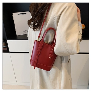 Detail of red leather bucket bag with dual handles and gold-tone hardware for women