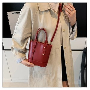 Detail of red bucket bag with gold studs on a model wearing a beige trench coat